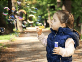 Little girl blowing bubbles outside